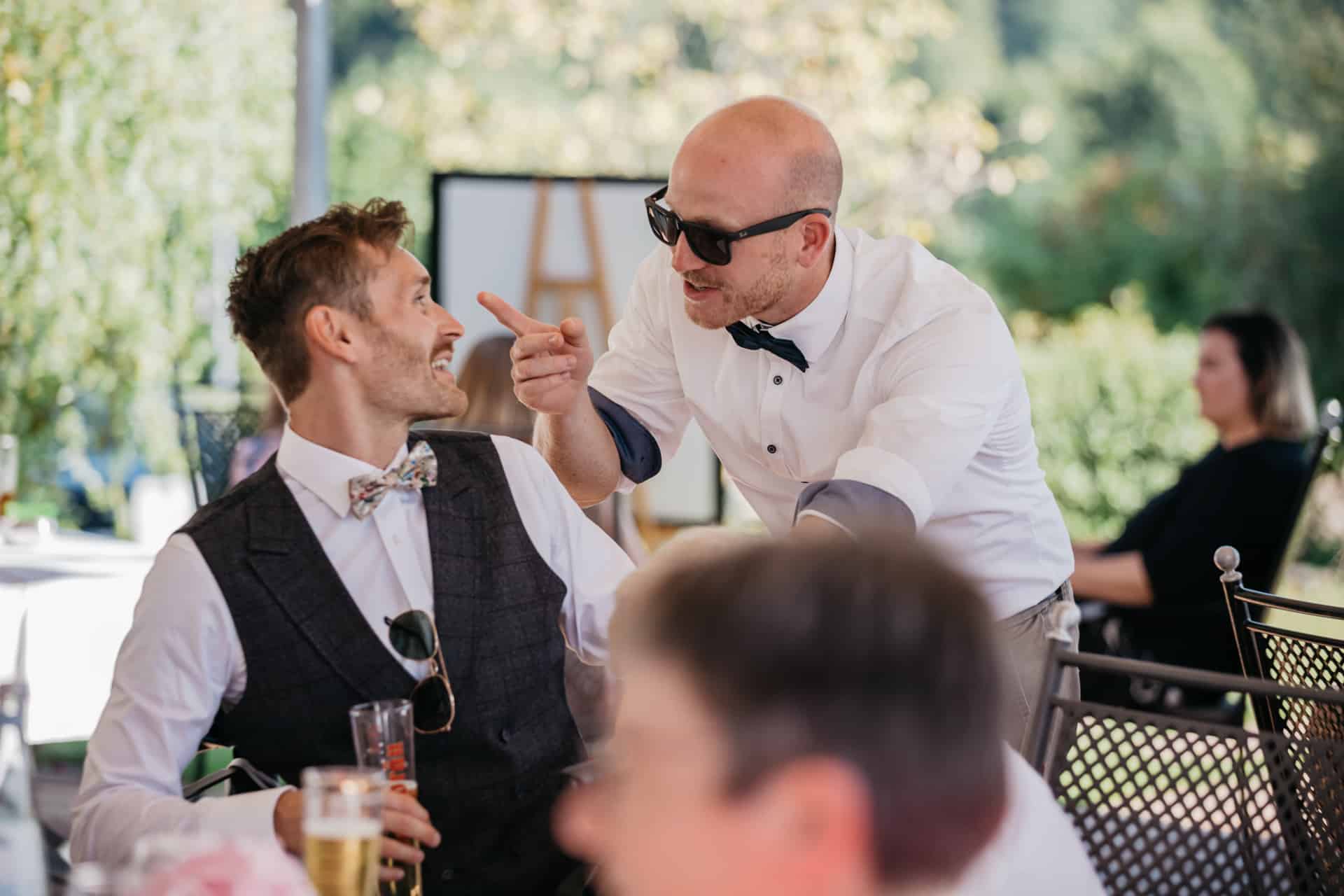 Bräutigam lacht mit einem Gast auf der Terrasse