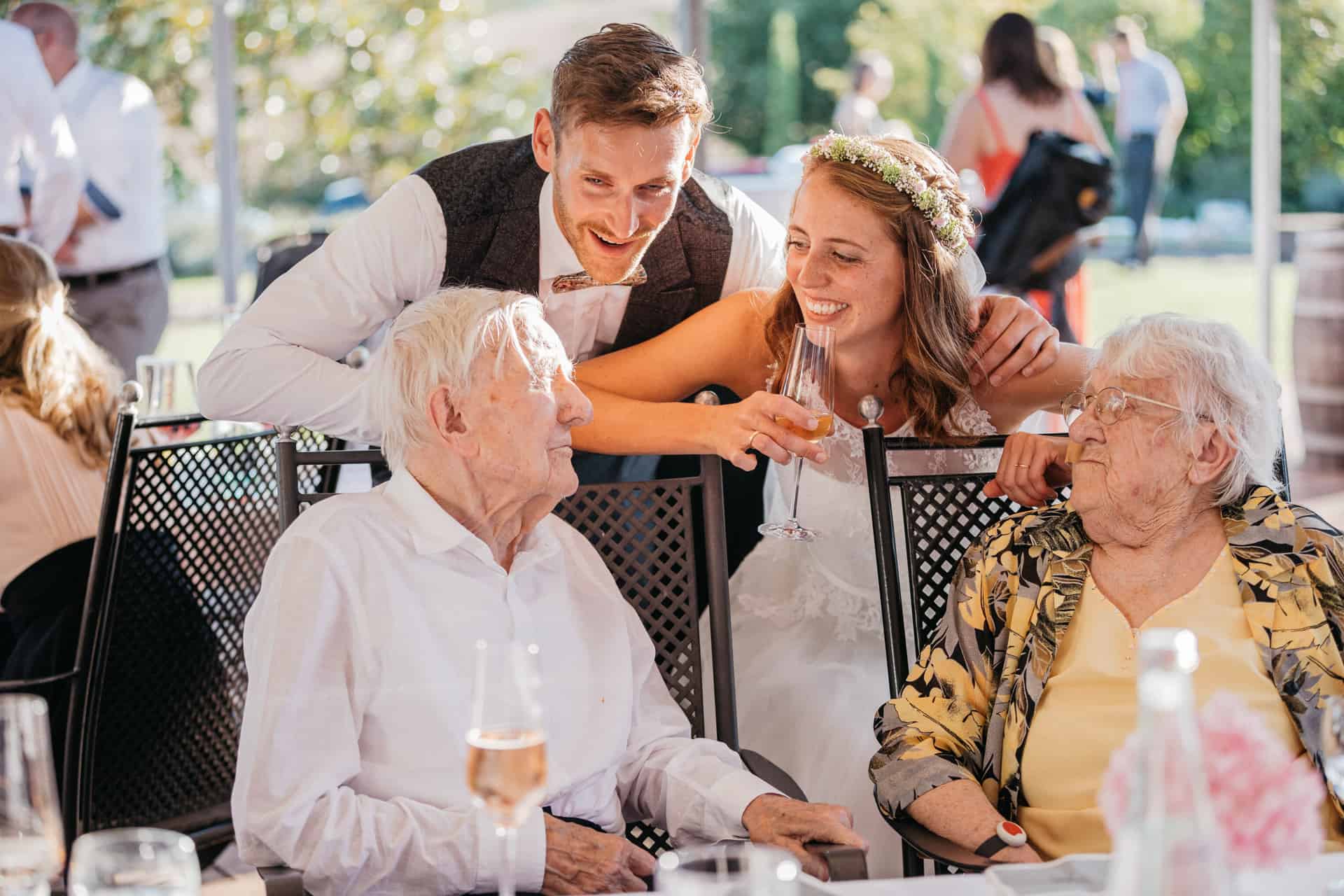 Bräutigam und Gäste beugen sich lachend zu einem älteren Gast