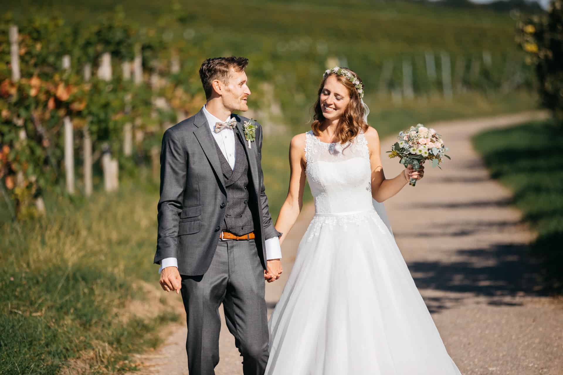Brautpaar spaziert Hand in Hand zwischen Reben