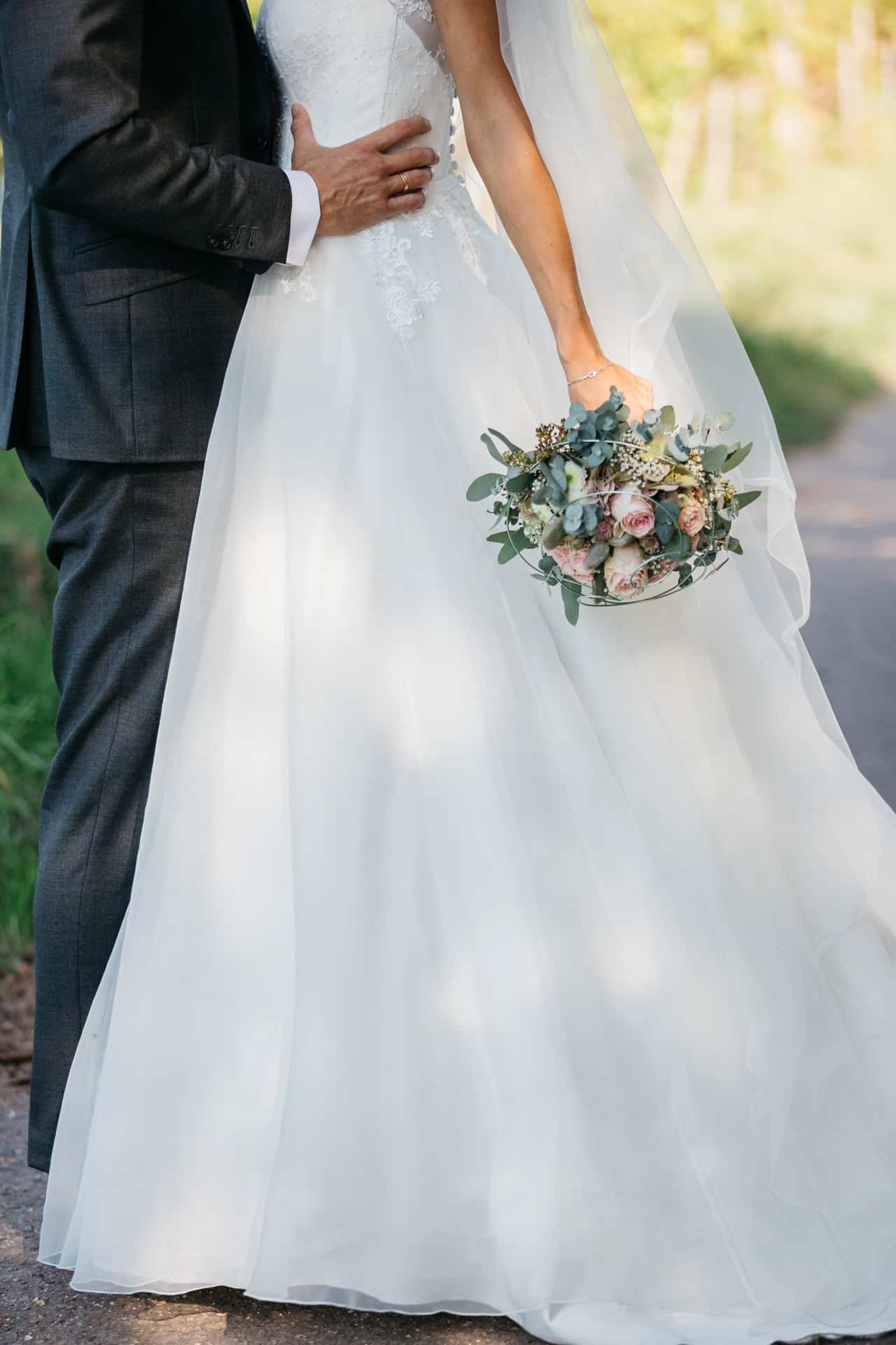 Detailaufnahme von Brautkleid und herabhängendem Blumenstrauß