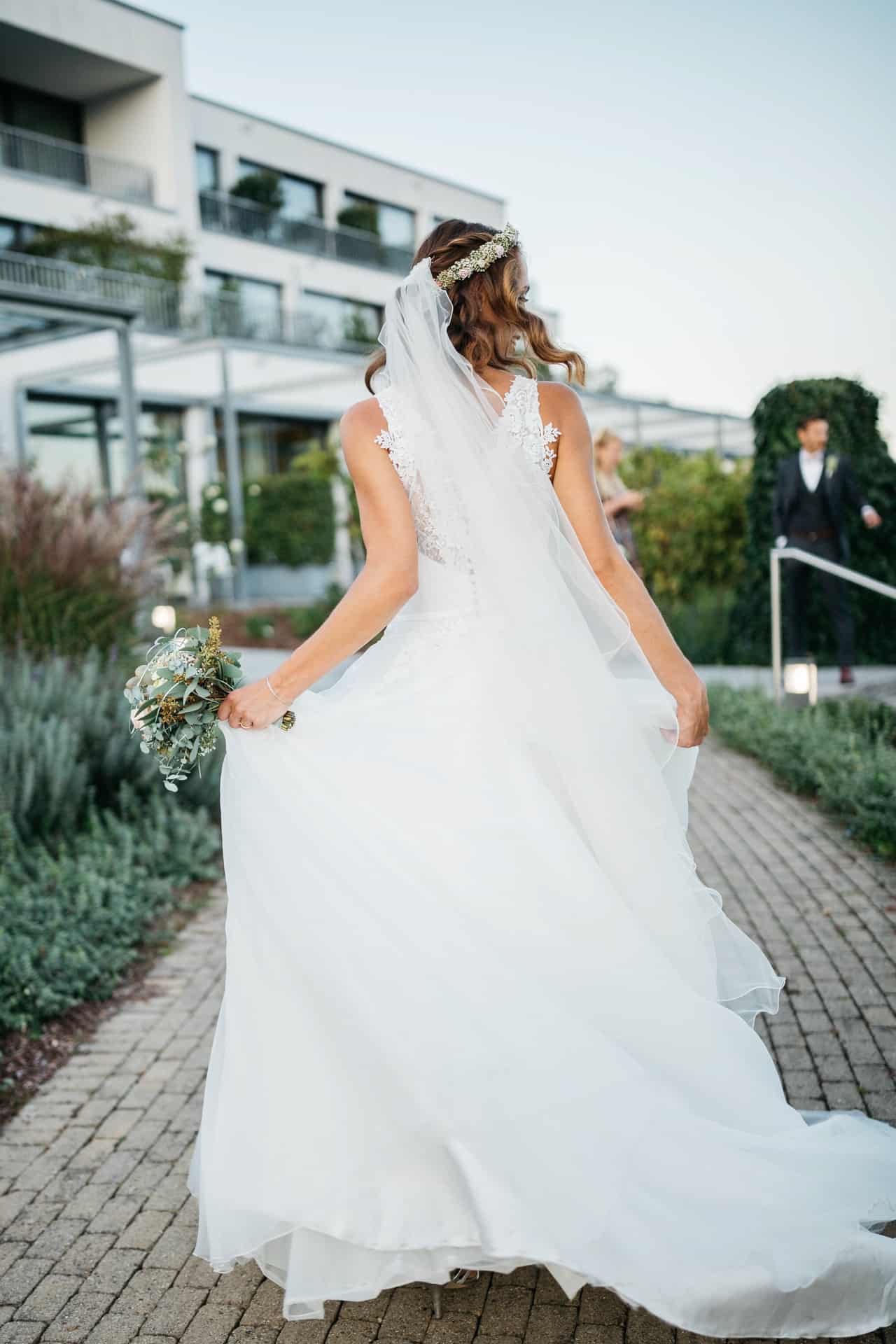 Braut steht mit ausgebreitetem Kleid vor der Hochzeitslocation