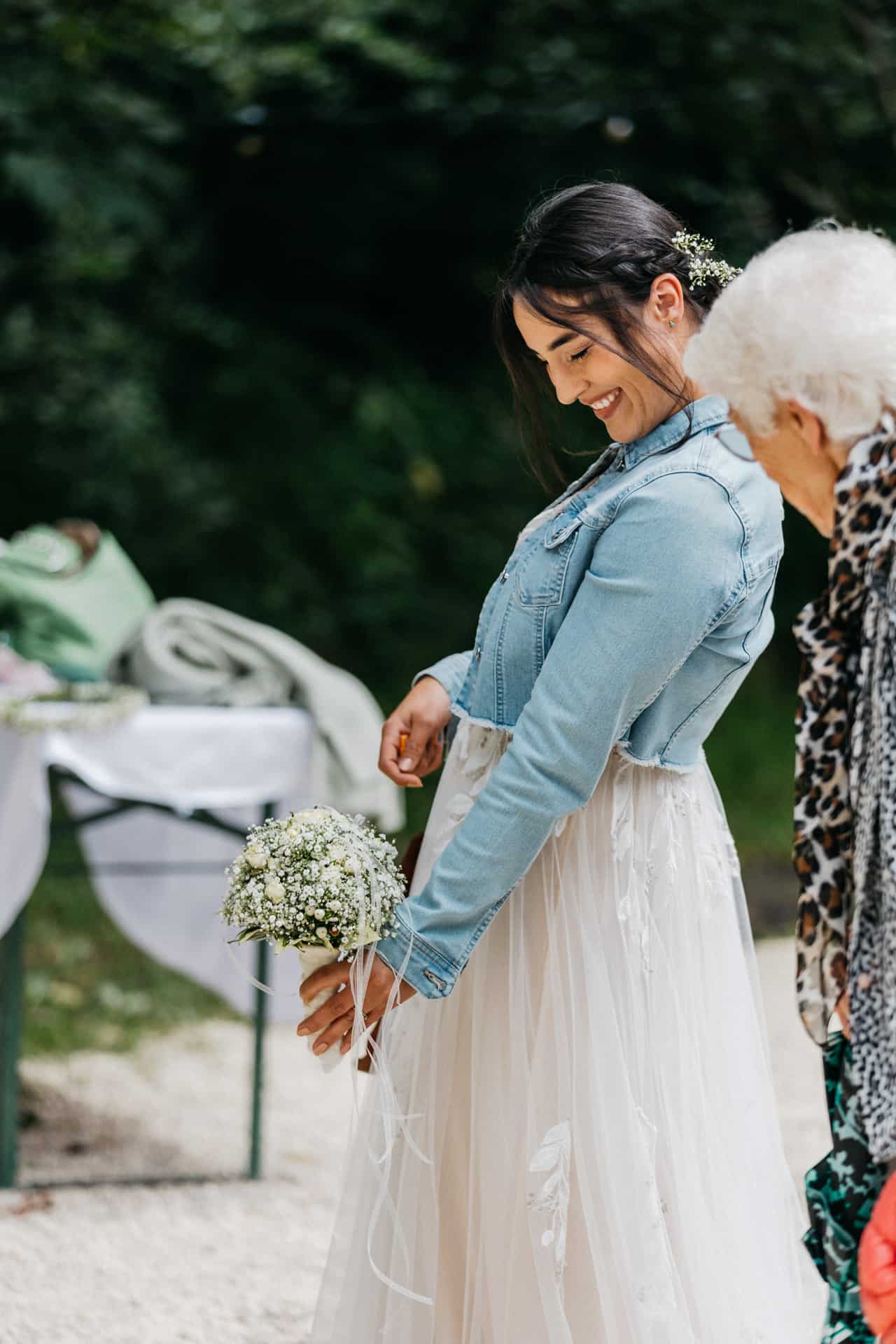 Die Braut trägt eine Jeansjacke und hält ihren Blumenstrauß.