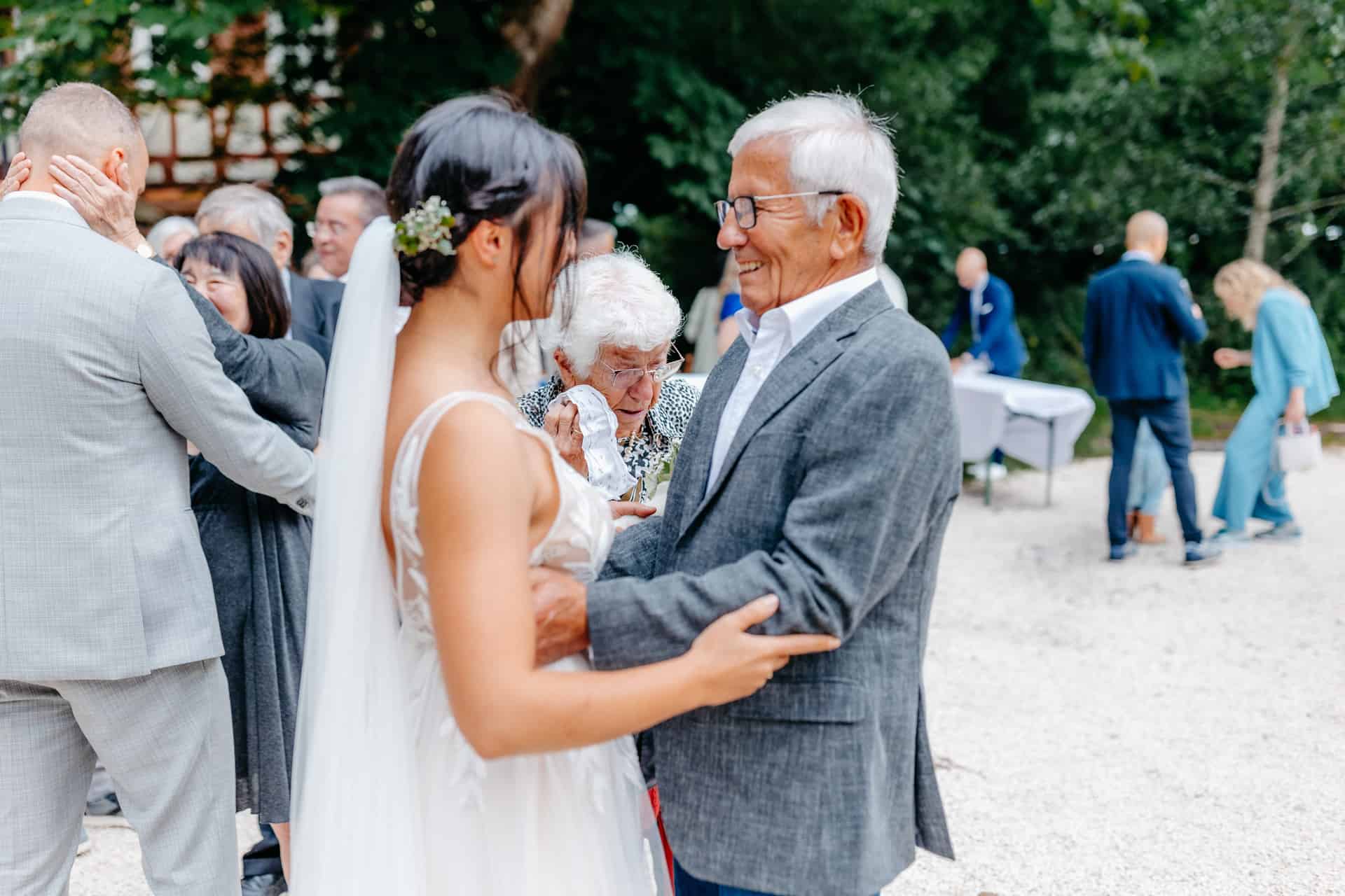 Die Braut begrüßt einen älteren Hochzeitsgast im Hof der Hagmühle.