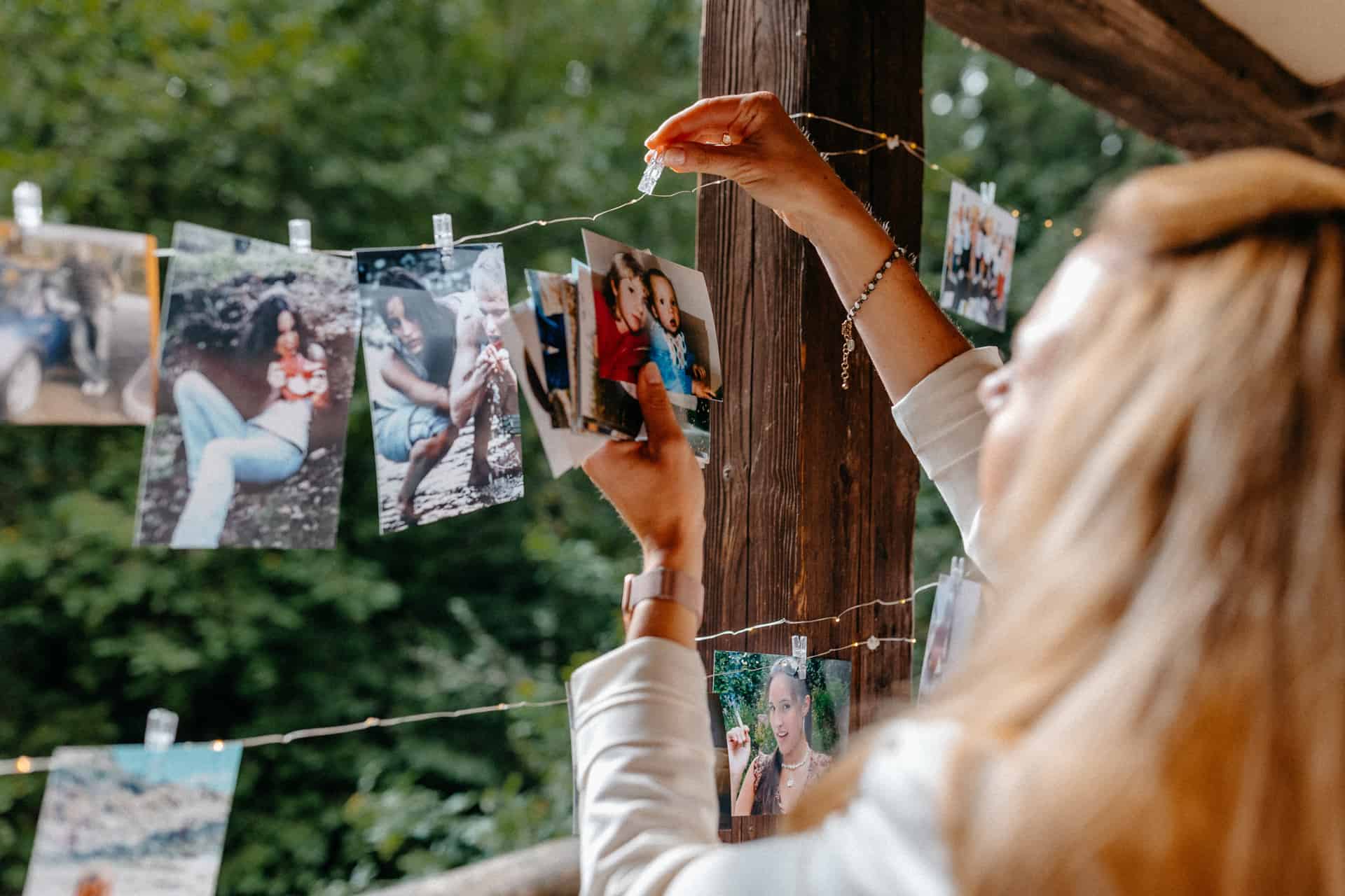 Eine Hochzeitsgästin betrachtet Fotos, die an einer Schnur befestigt sind.