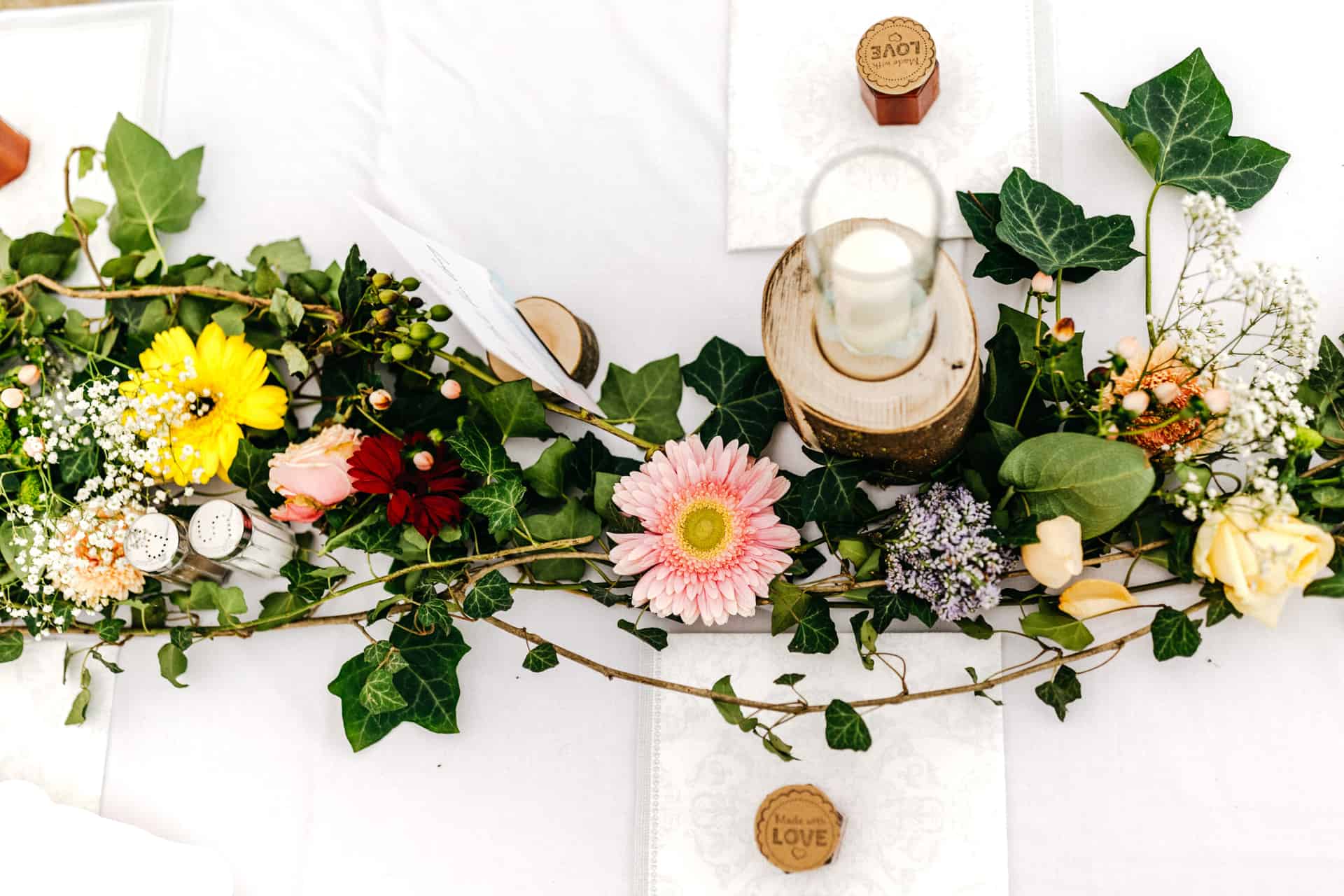 Blumendekoration und eine kleine Uhr auf dem gedeckten Hochzeitstisch.