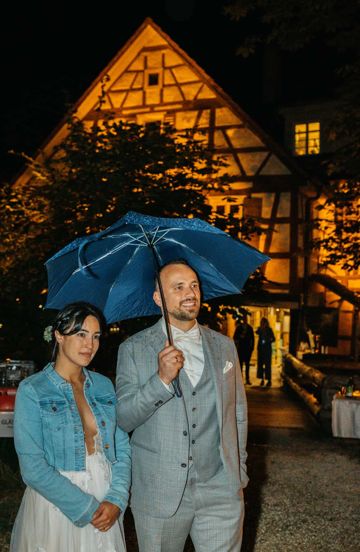 Das Brautpaar steht unter einem Regenschirm vor der abends beleuchteten Hagmühle.