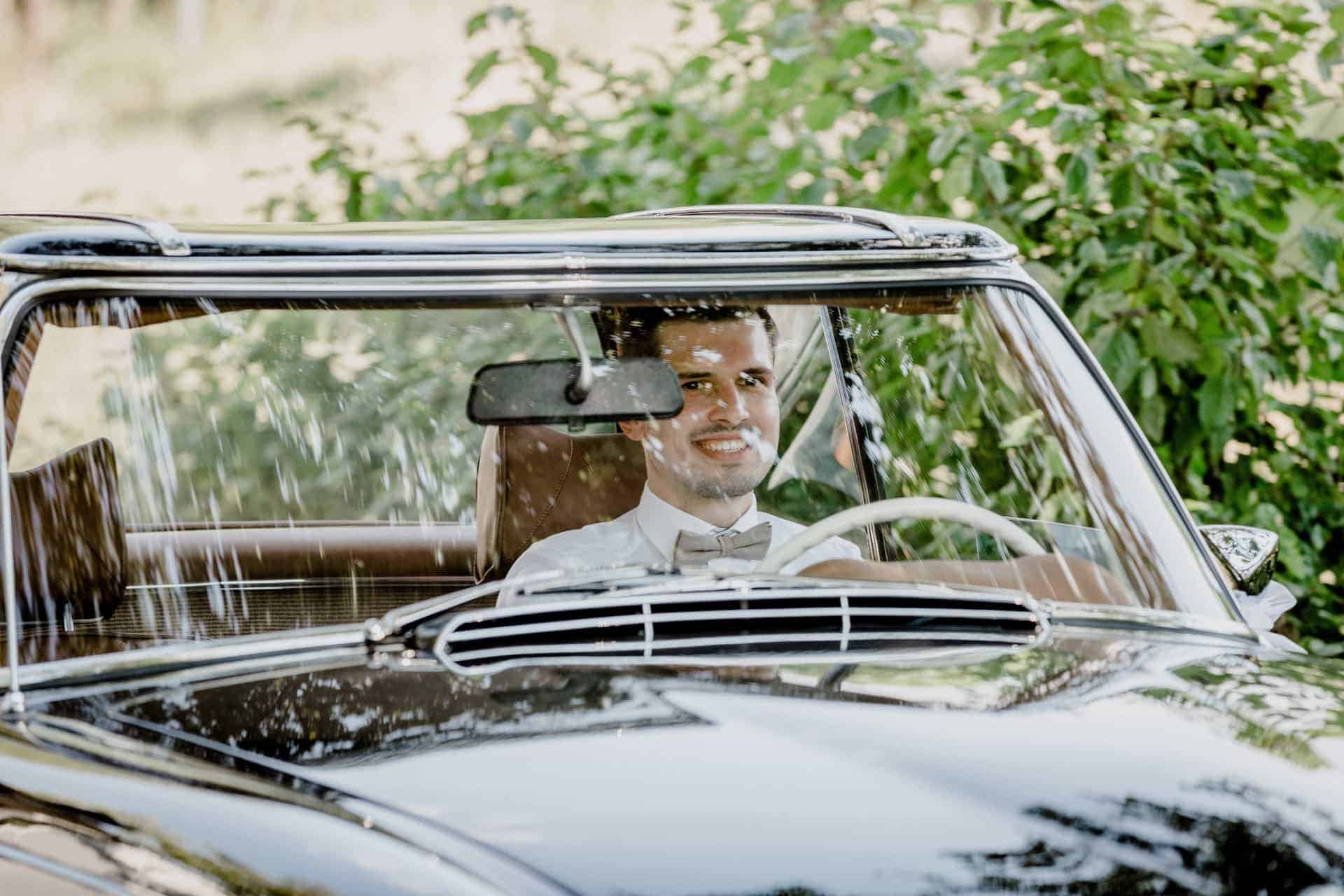 Ein Mann sitzt am Steuer eines offenen Oldtimers.
