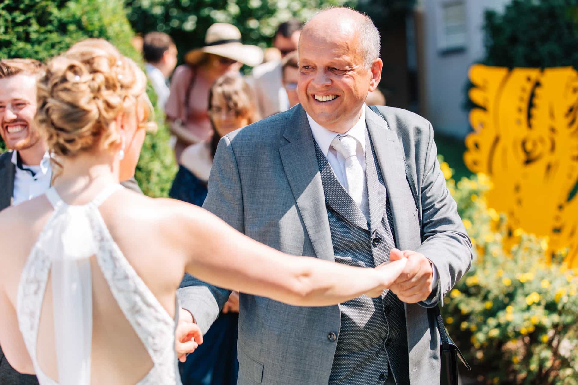 Braut begrüßt einen älteren Gast mit ausgestreckten Händen