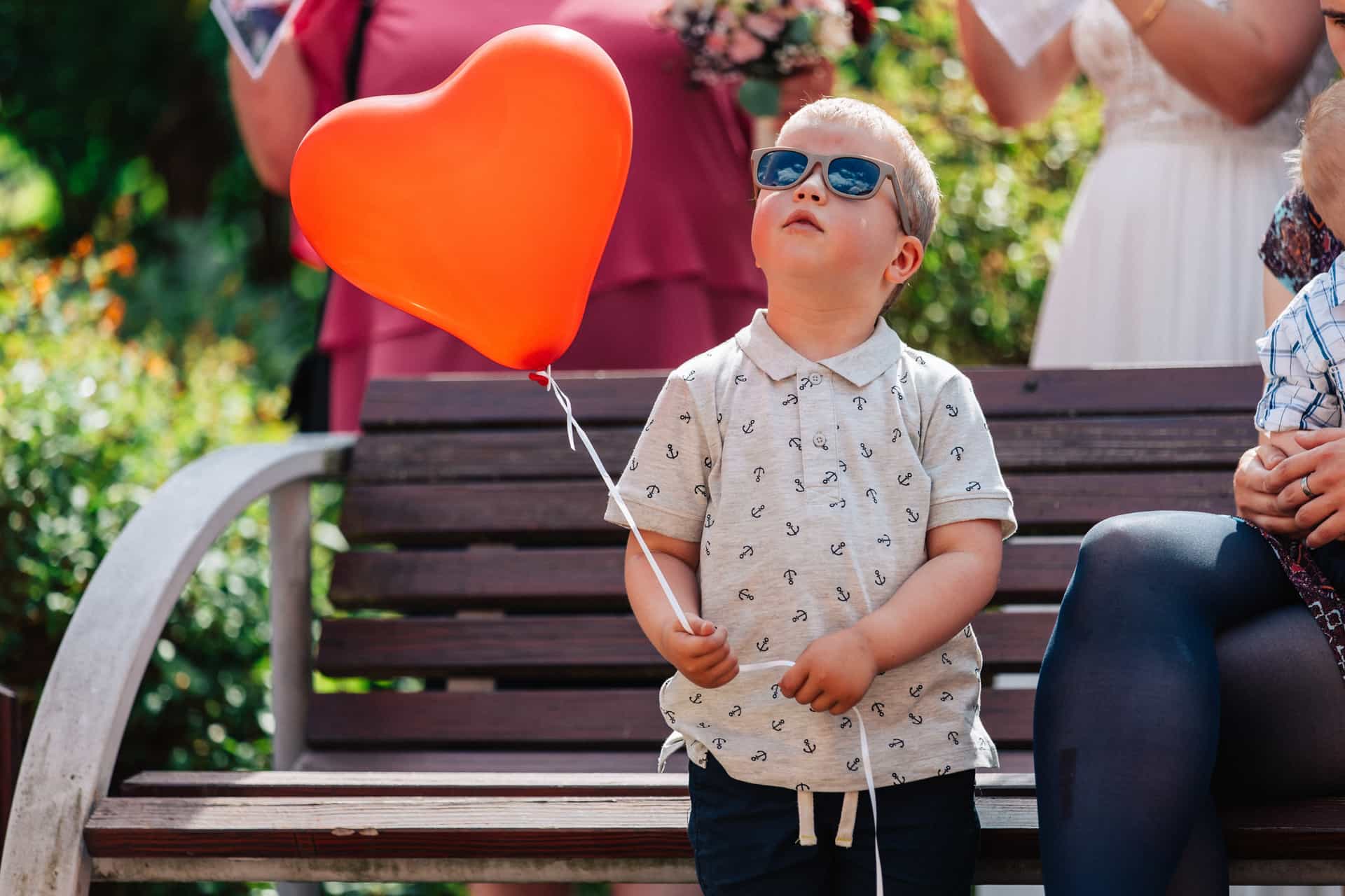 Ein Kind hält einen orangefarbenen Herzluftballon.