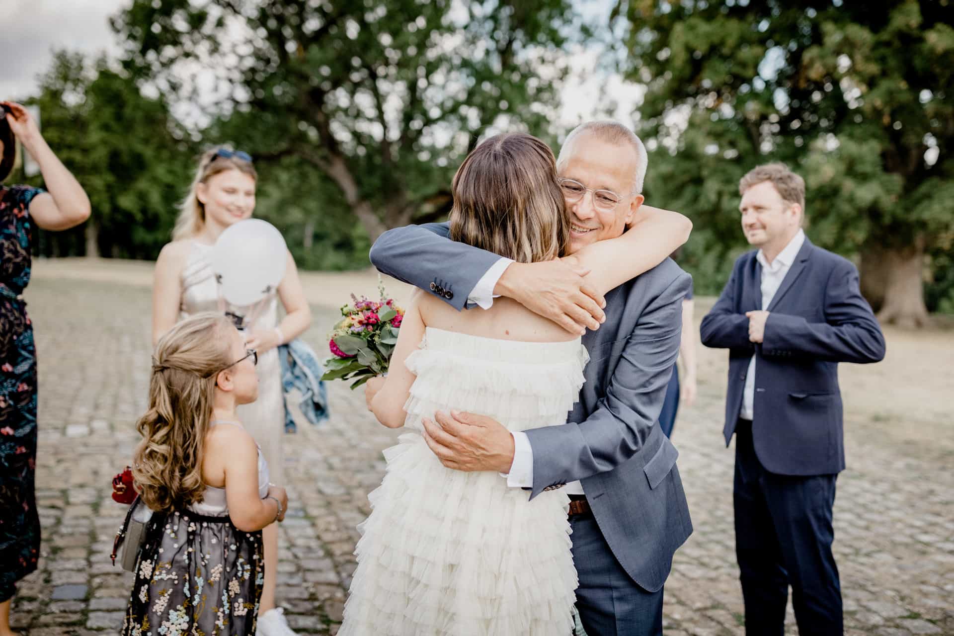 Braut umarmt einen älteren Gast unter den Bäumen
