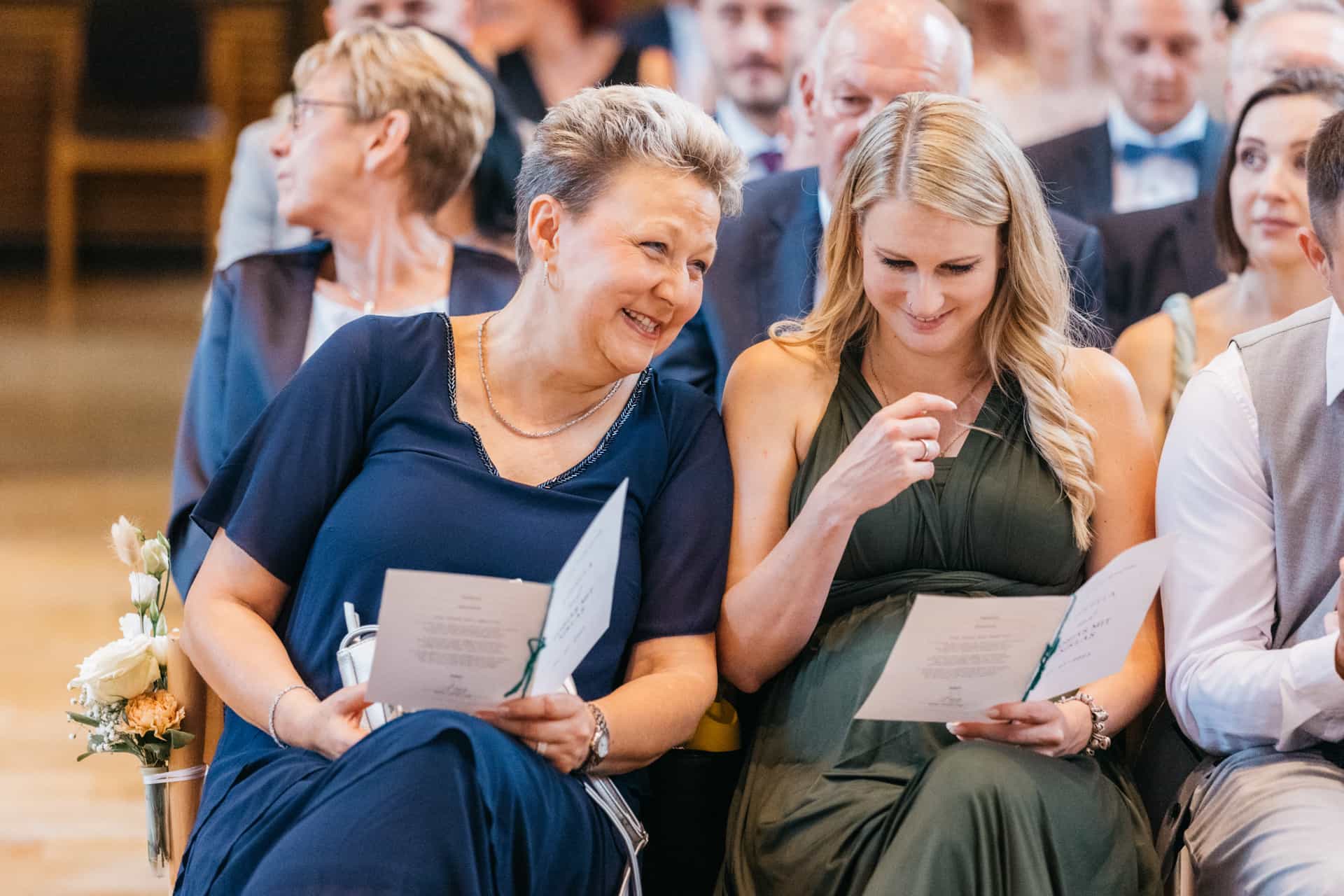Zwei Hochzeitsgäste lesen das Trauprogramm in der Kirchenbank