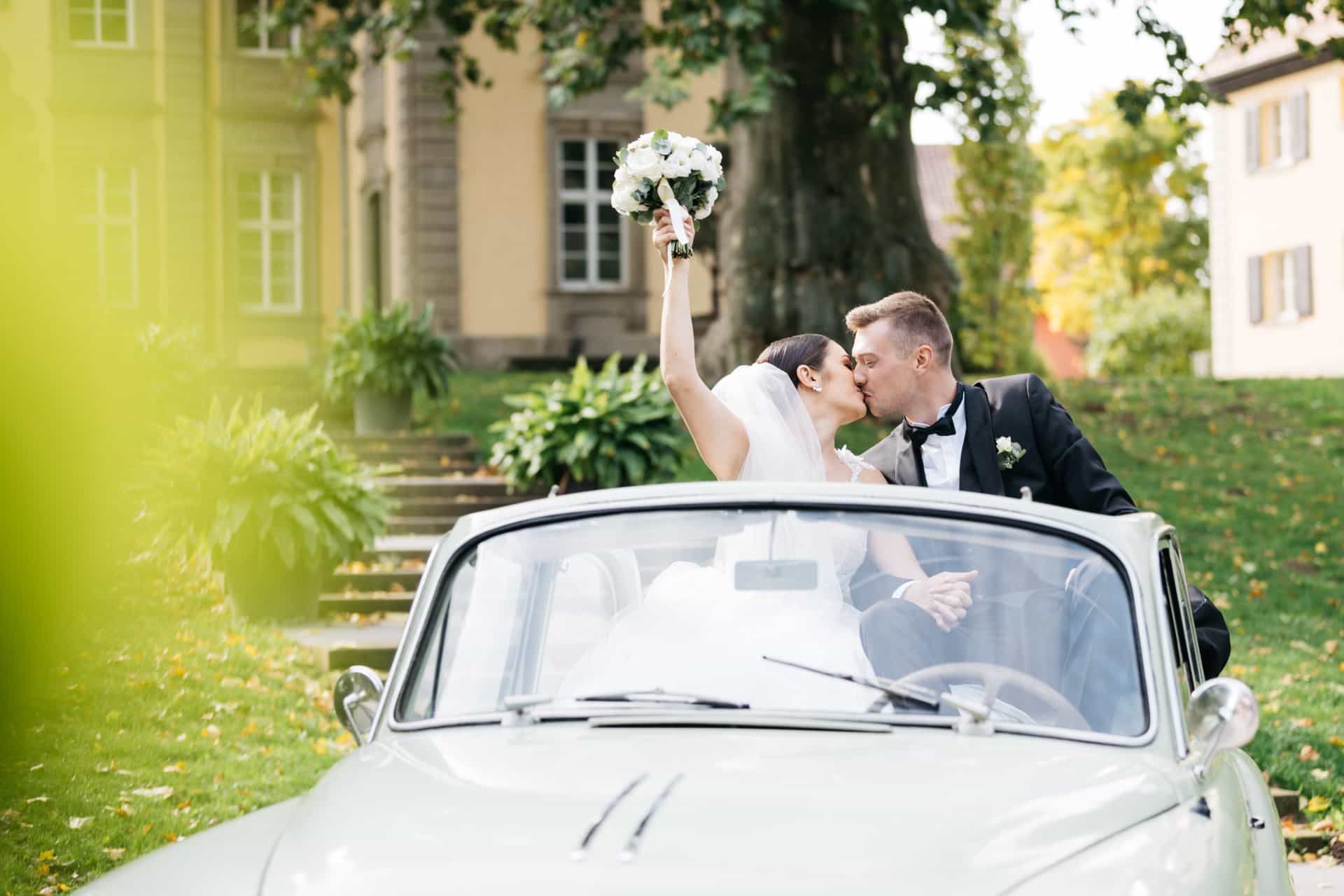 Brautpaar küsst sich im offenen Hochzeitswagen