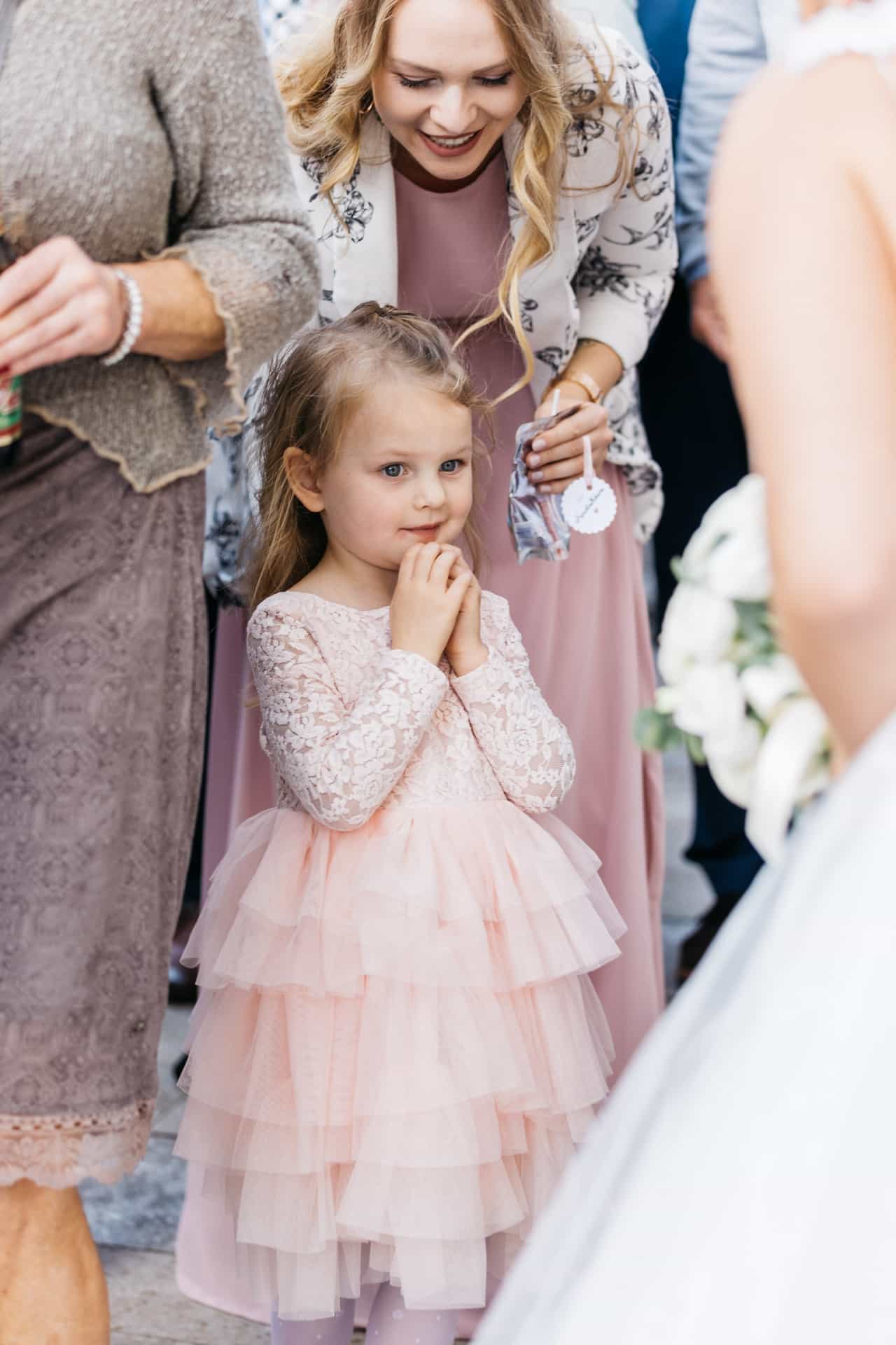 Kleines Mädchen im rosa Kleid zwischen Hochzeitsgästen