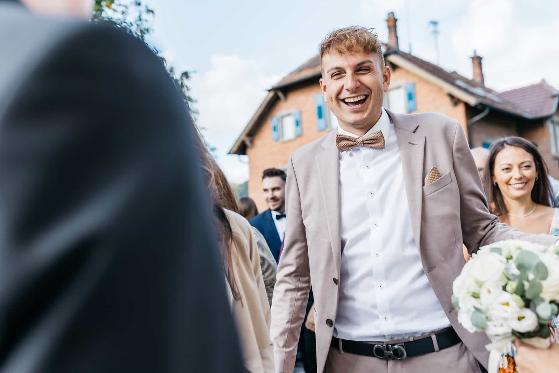 Ein Hochzeitsgast lacht beim Empfang vor der Kirche.