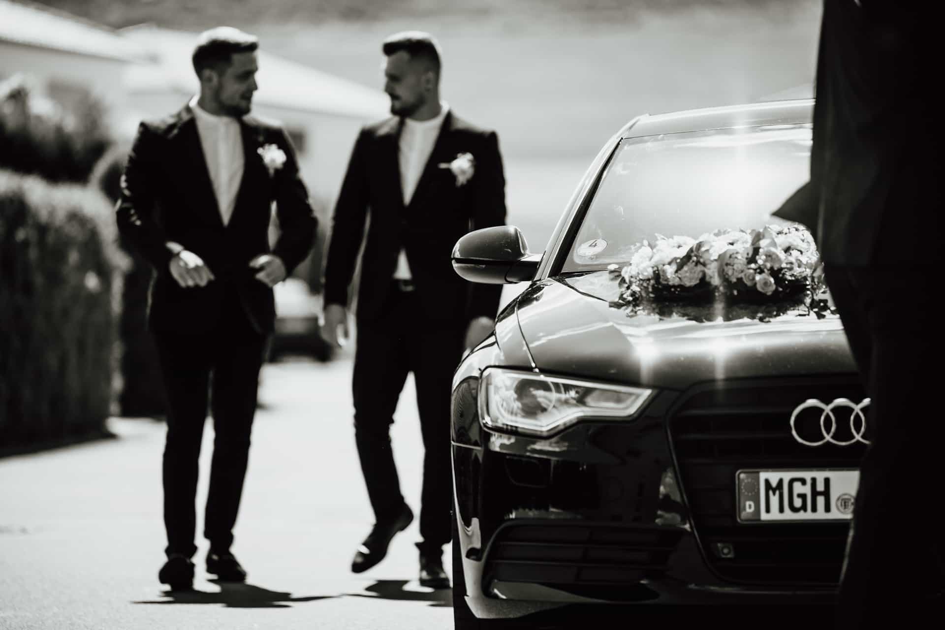 Bräutigam und Begleiter stehen am Hochzeitswagen in Schwarz-Weiß