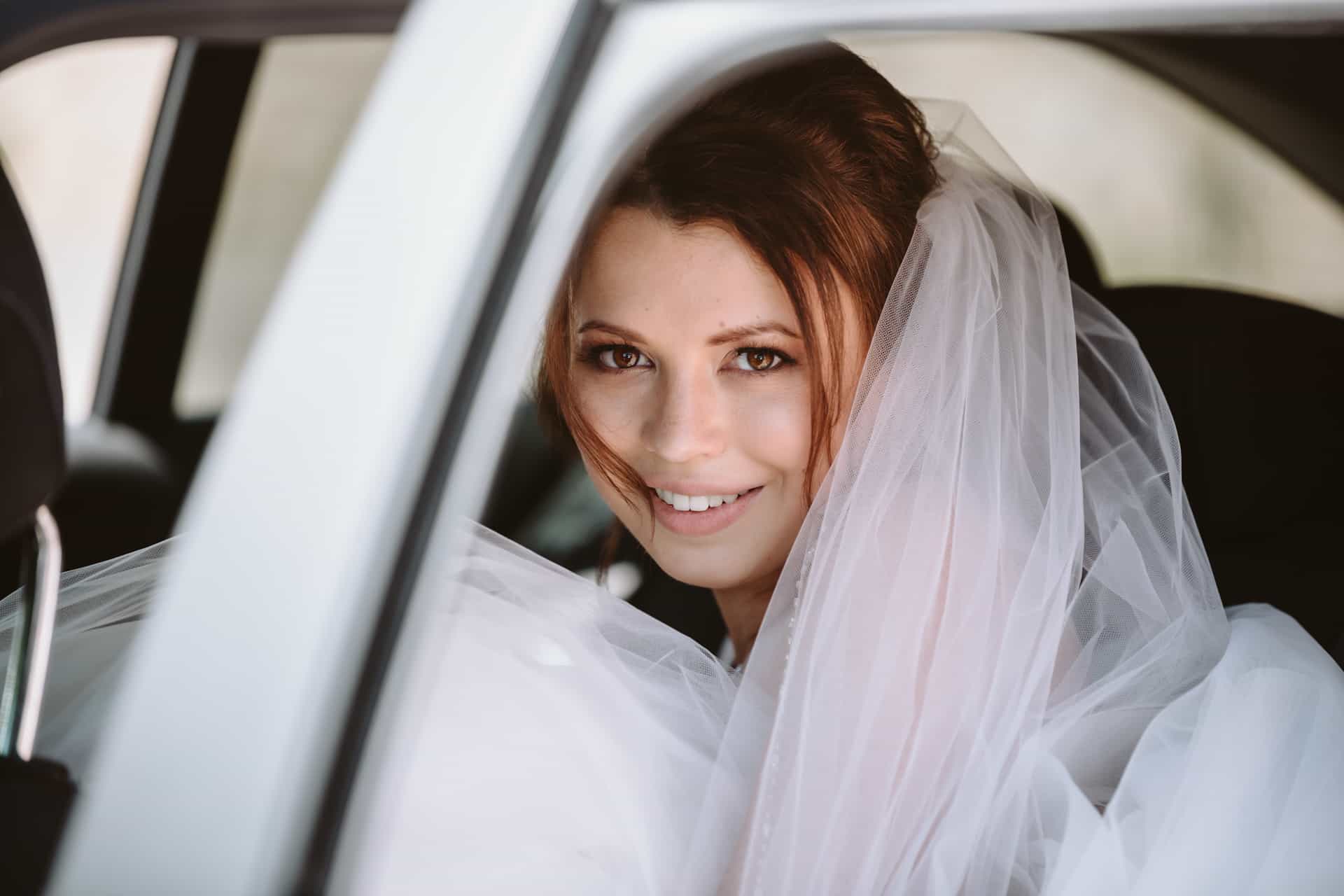 Braut blickt lächelnd aus dem Hochzeitswagen