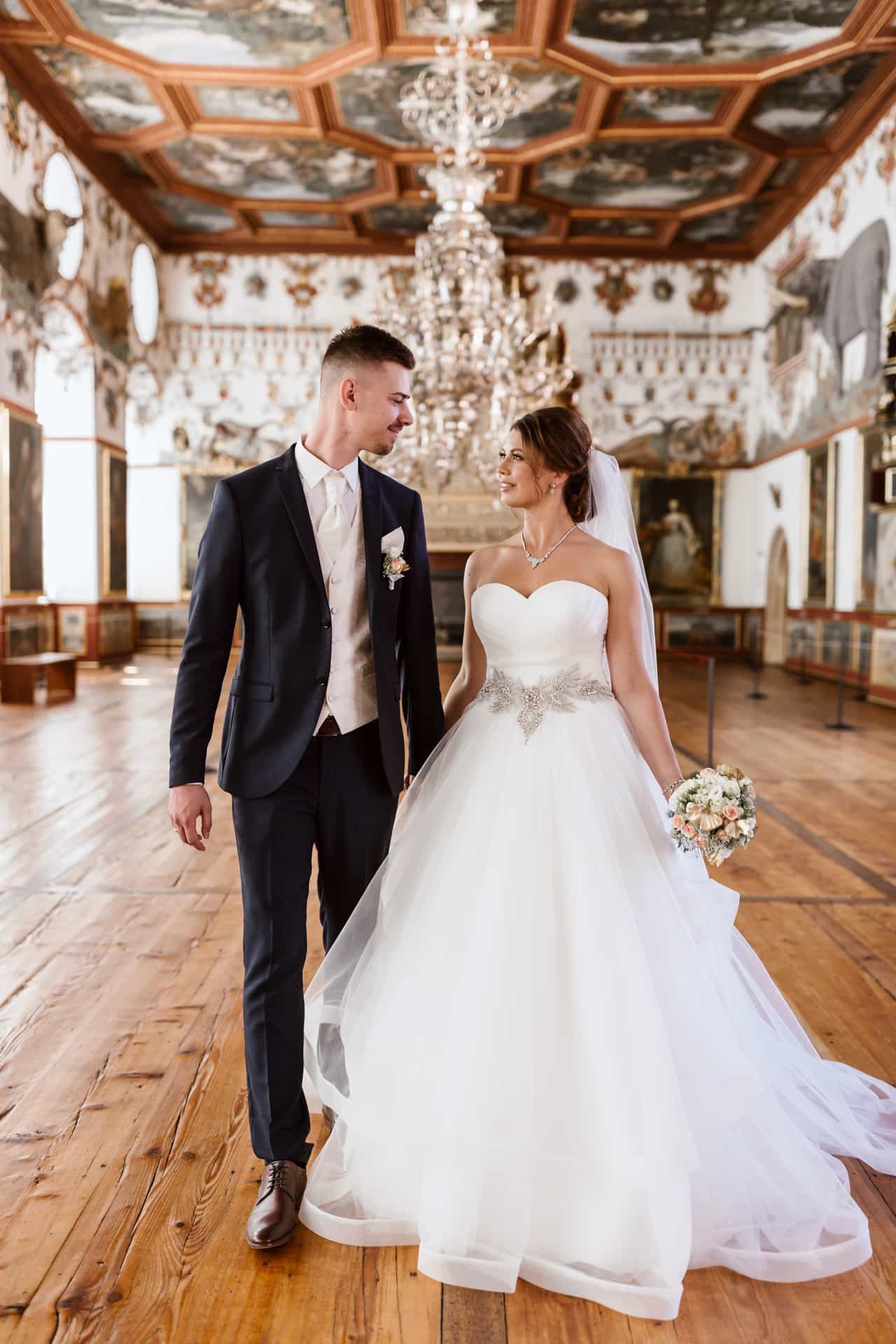 Anja und Artur gehen Hand in Hand durch den prunkvollen Saal von Schloss Weikersheim.